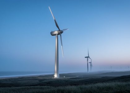 Low-angle view of a four-blade wind turbine in a wind farm at dusk under a blue-gray sky.